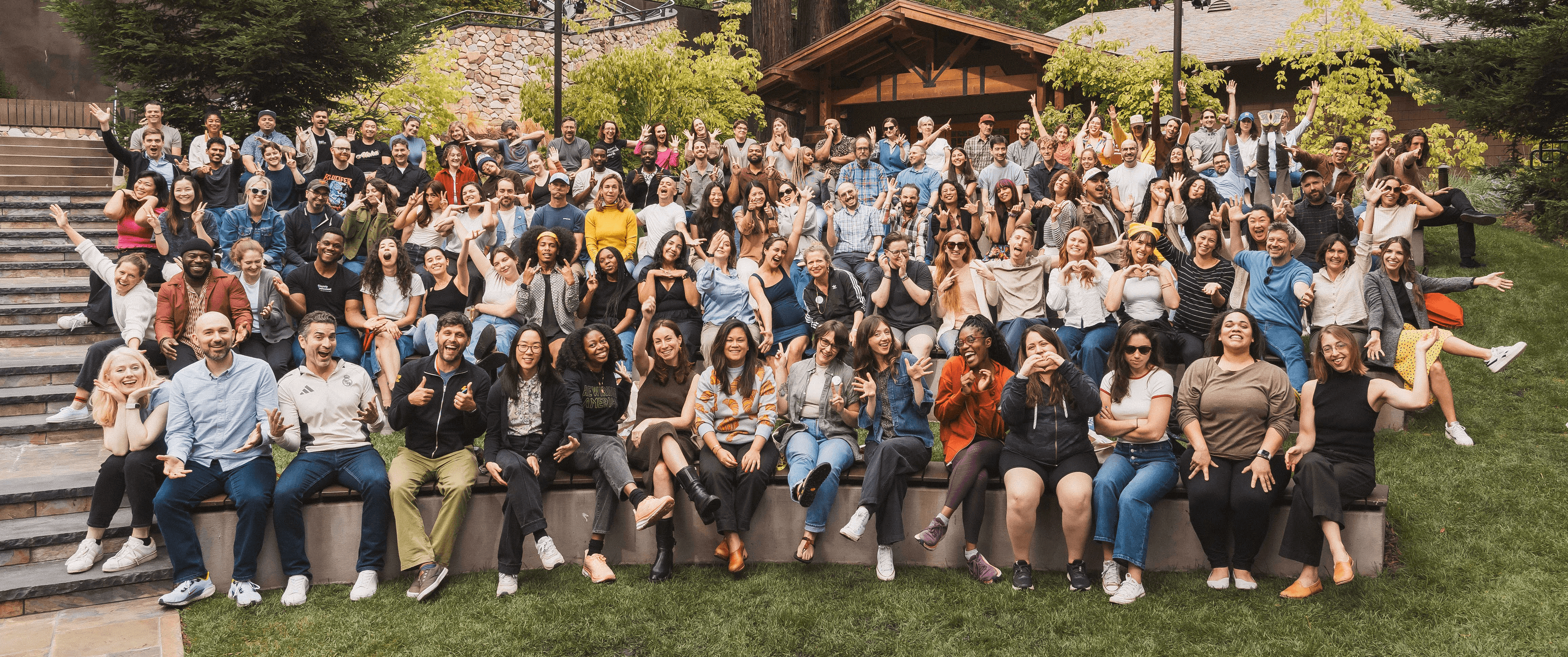 Group photo of the Rewiring America team seated in an outdoor amphitheater. There are 5 rows of people making various 'funny' poses, such as sticking their arms out, peace signs, and pointing at each other.