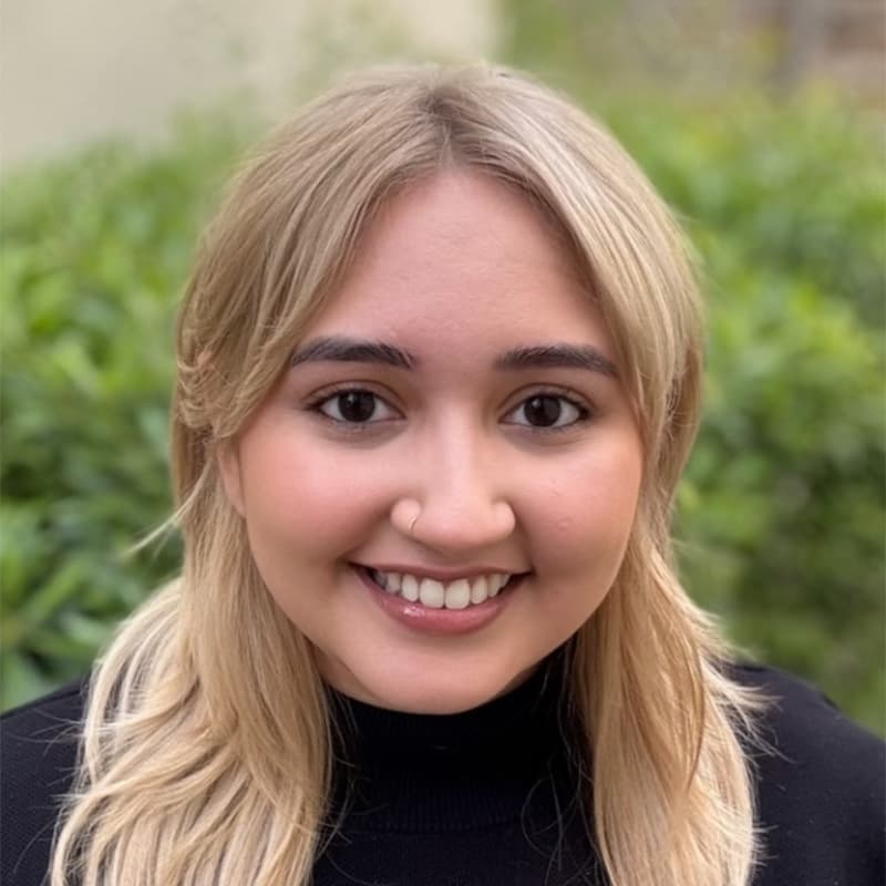 Headshot of Kavina del Monte, who is smiling and has long blonde hair. She is wearing a black turtleneck.