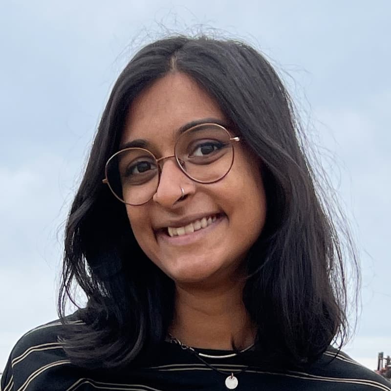 Headshot of Christine George, who is smiling, wears glasses, has shoulder length black hair. She is wearing a striped black shirt.