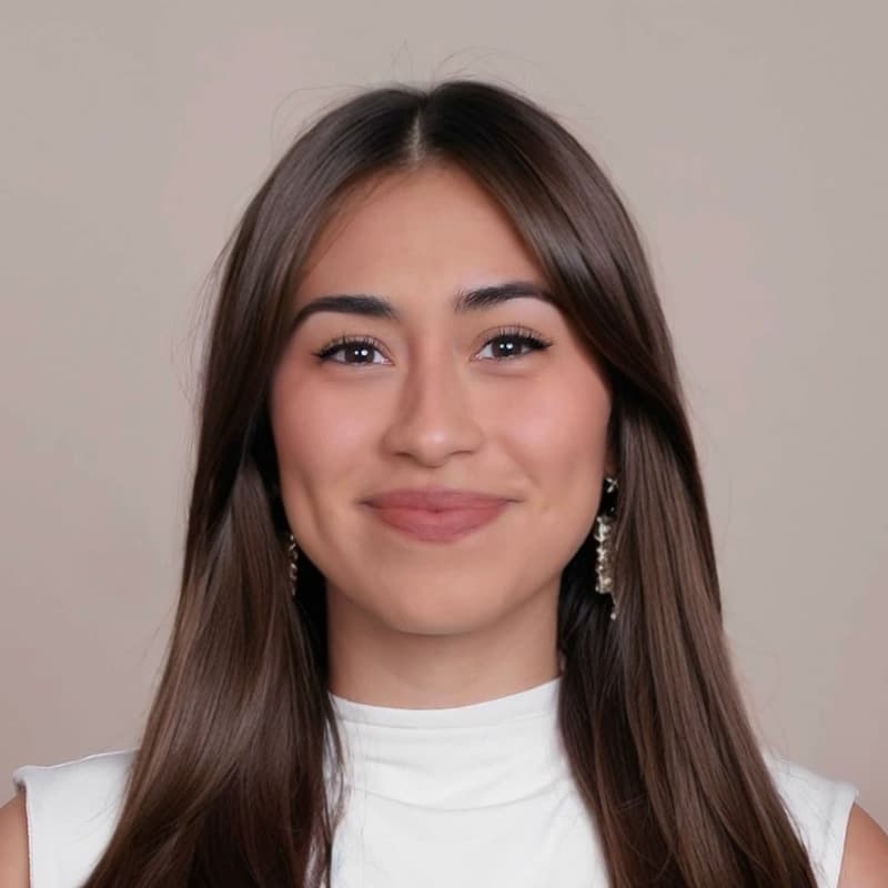 Headshot of Yazmyn Pelaez, who is slightly smiling and has long straight brown hair. She is wearing a white sleeveless mockneck top.