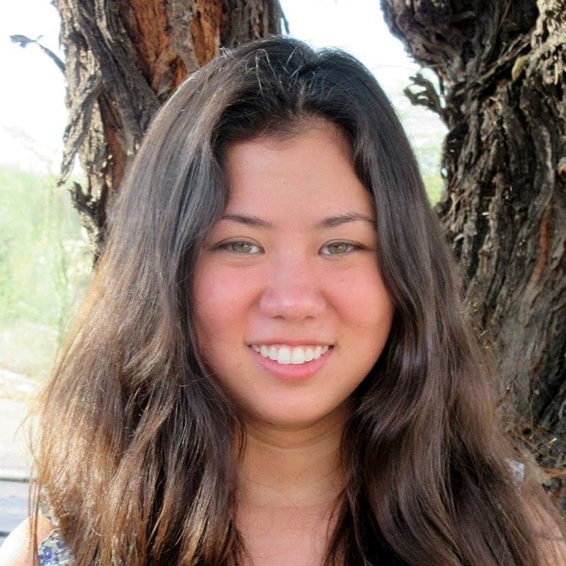 Headshot of Bonnie Ishiguro, who is smiling and has long wavy light brown hair. She stands in front of two trees.