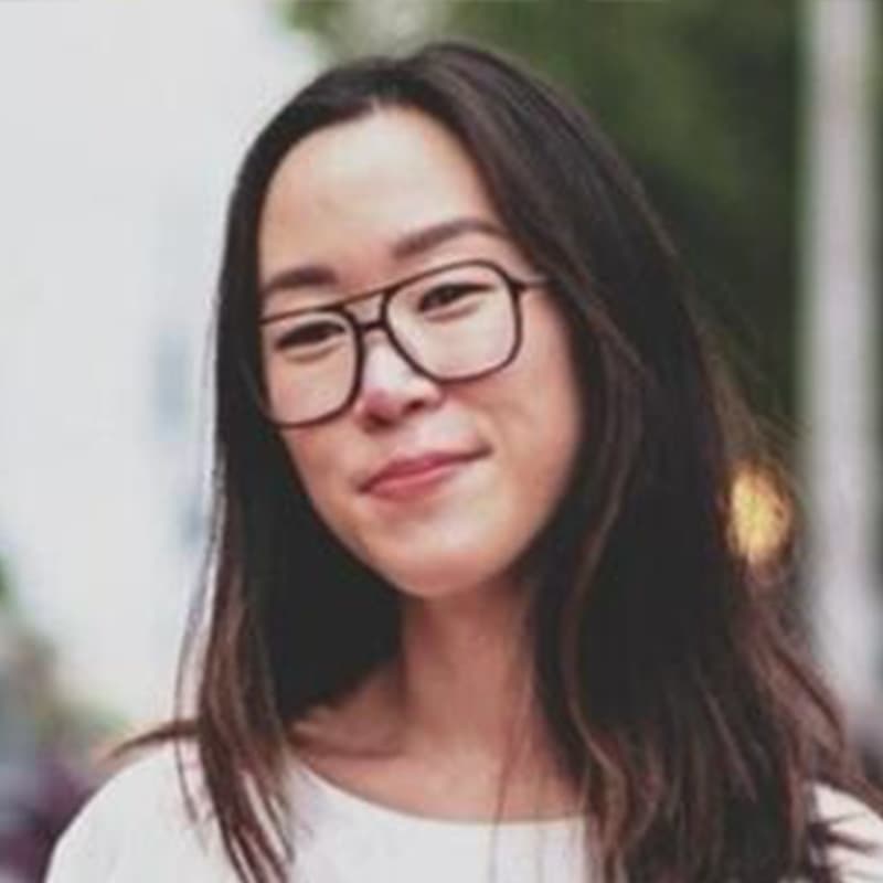 Headshot of Anna Hovland, who is slightly smiling and wears black frame glasses. She has straight black hair and wears a white long sleeve top.