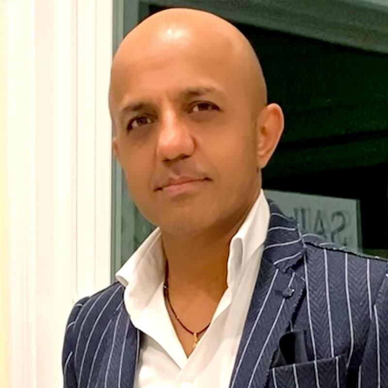 Headshot of Sridhar Solur, who stares forward. He is bald and wears a navy striped suit and an white collared shirt.