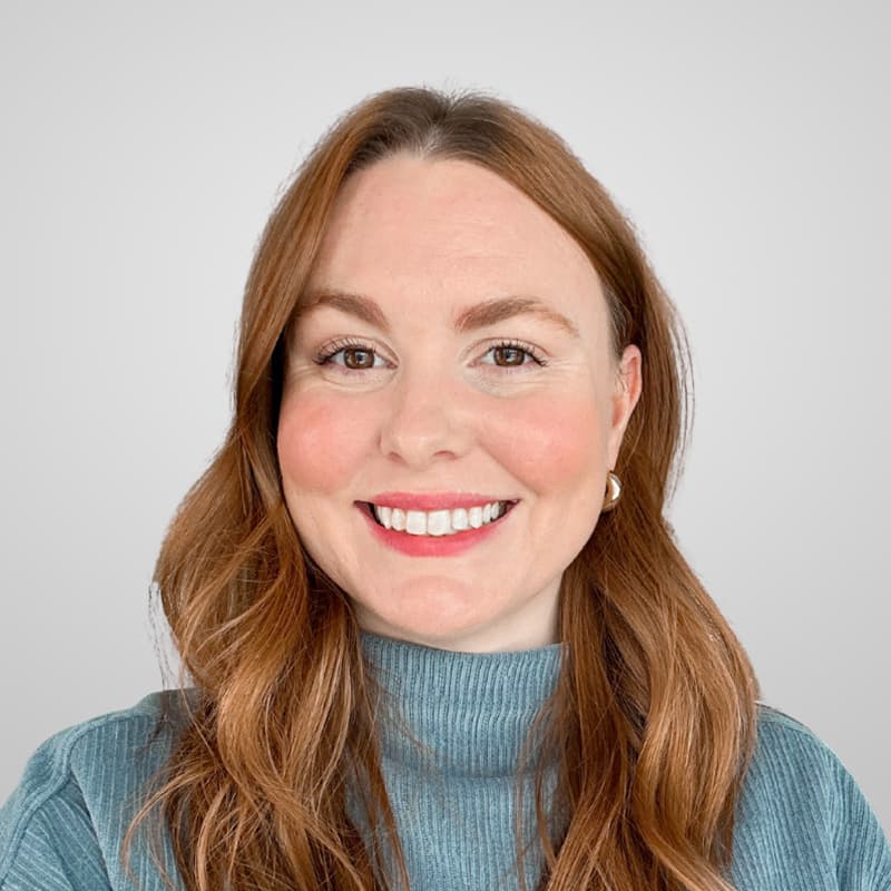 Headshot of Blair Brown, who is smiling and has long wavy red hair. She is wearing a light blue turtleneck.